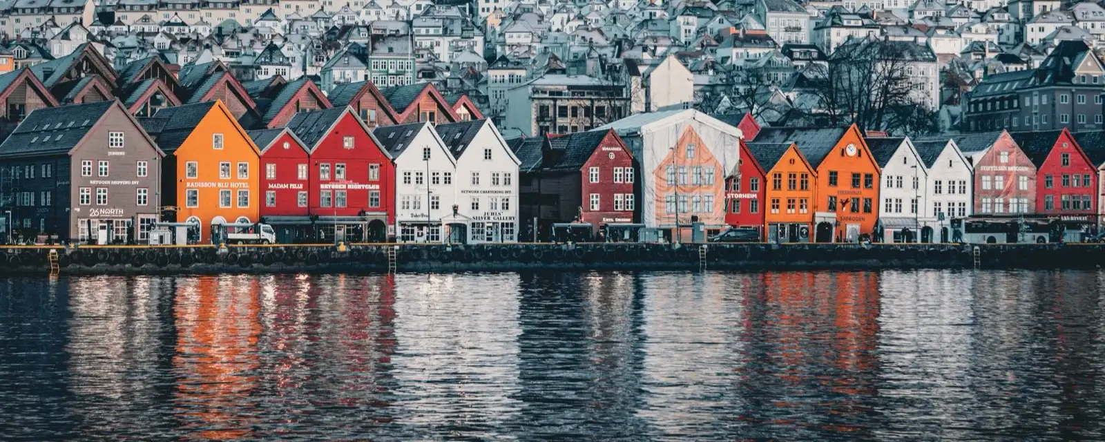 Bryggen i Bergen i skumringen, med fargerike trehus og speilbilder i vannet
